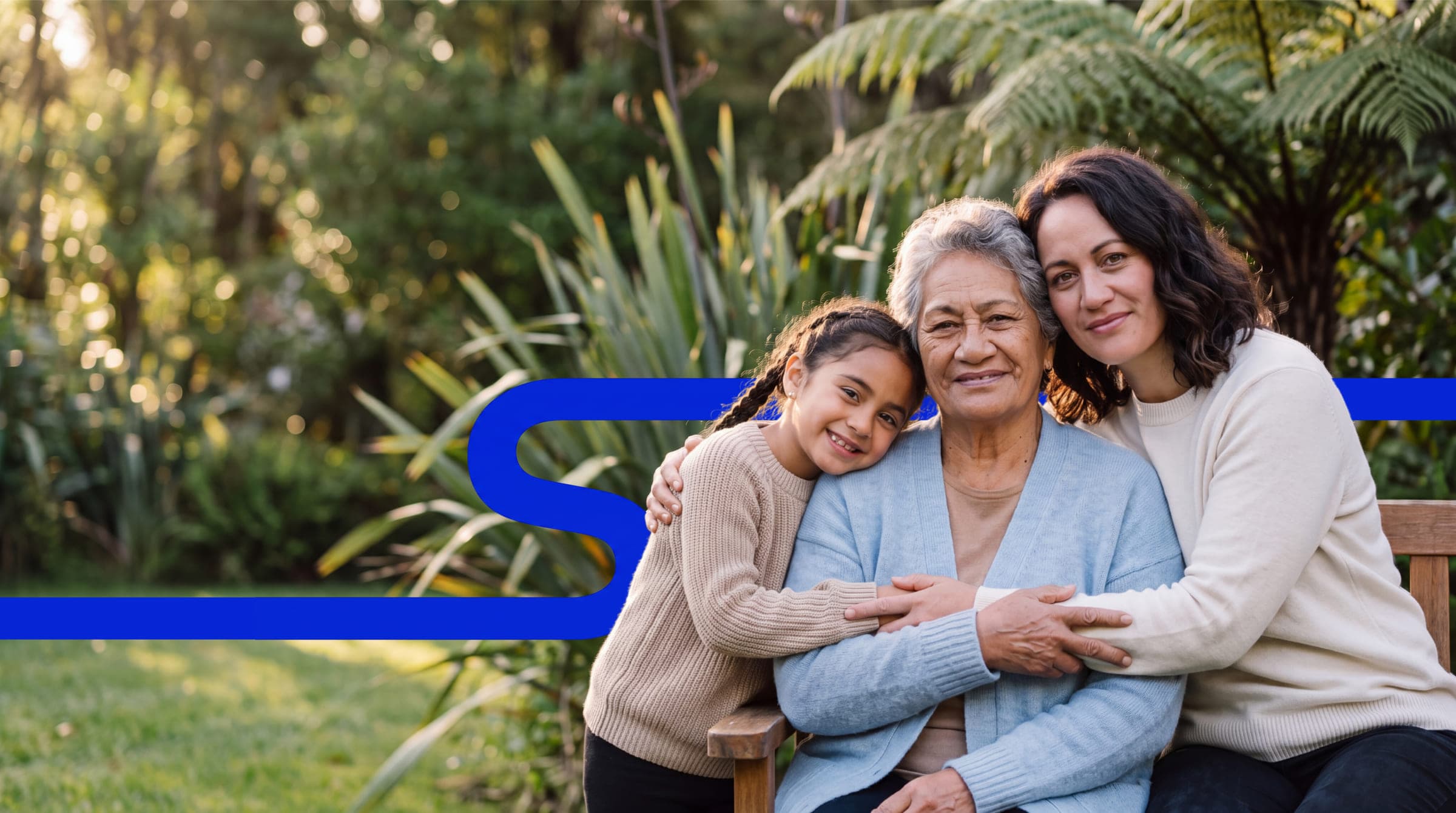 Three generations of one family sit together on a garden bench among tree ferns and flax, the Systemaize S line running across the frame behind them