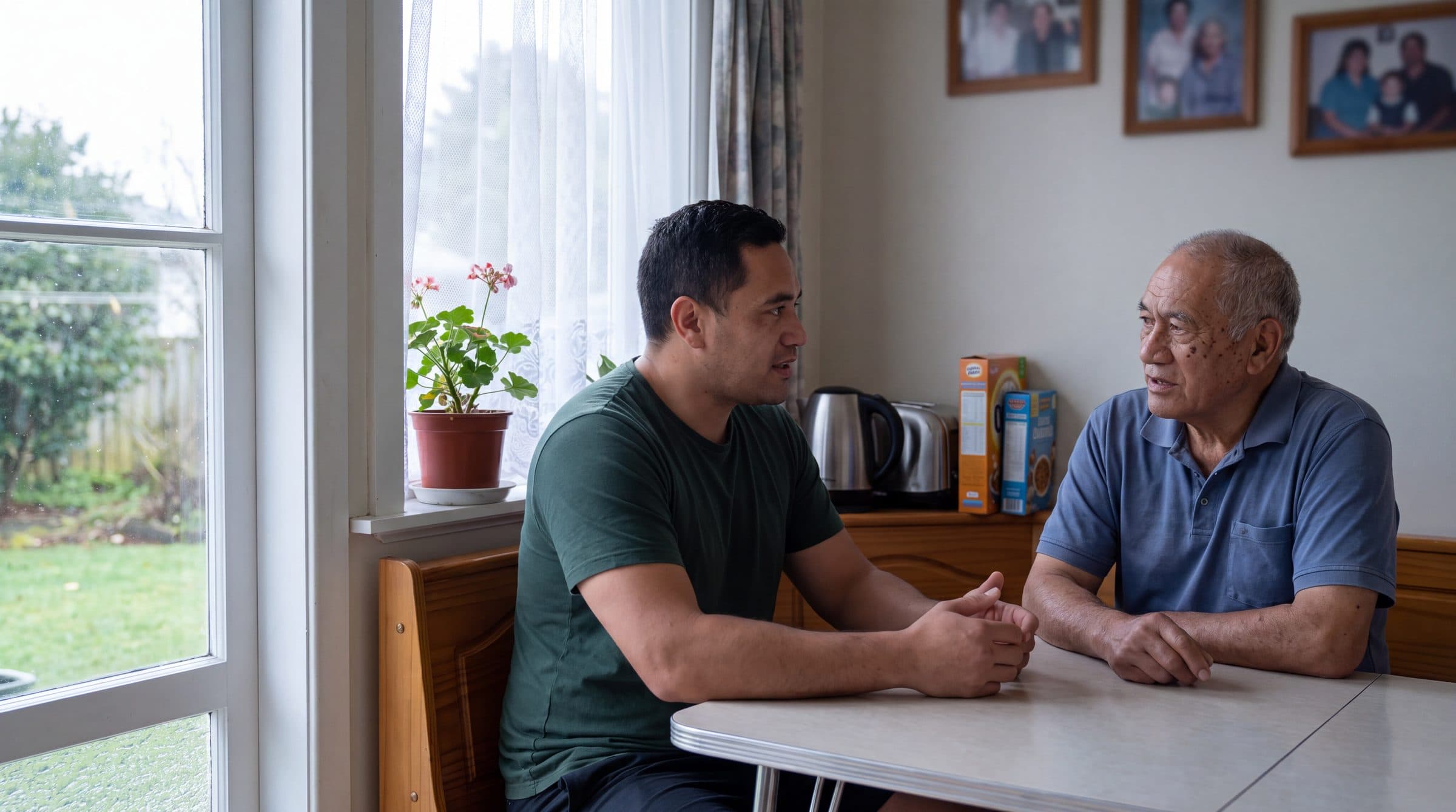 Two men talking across a kitchen table by the window