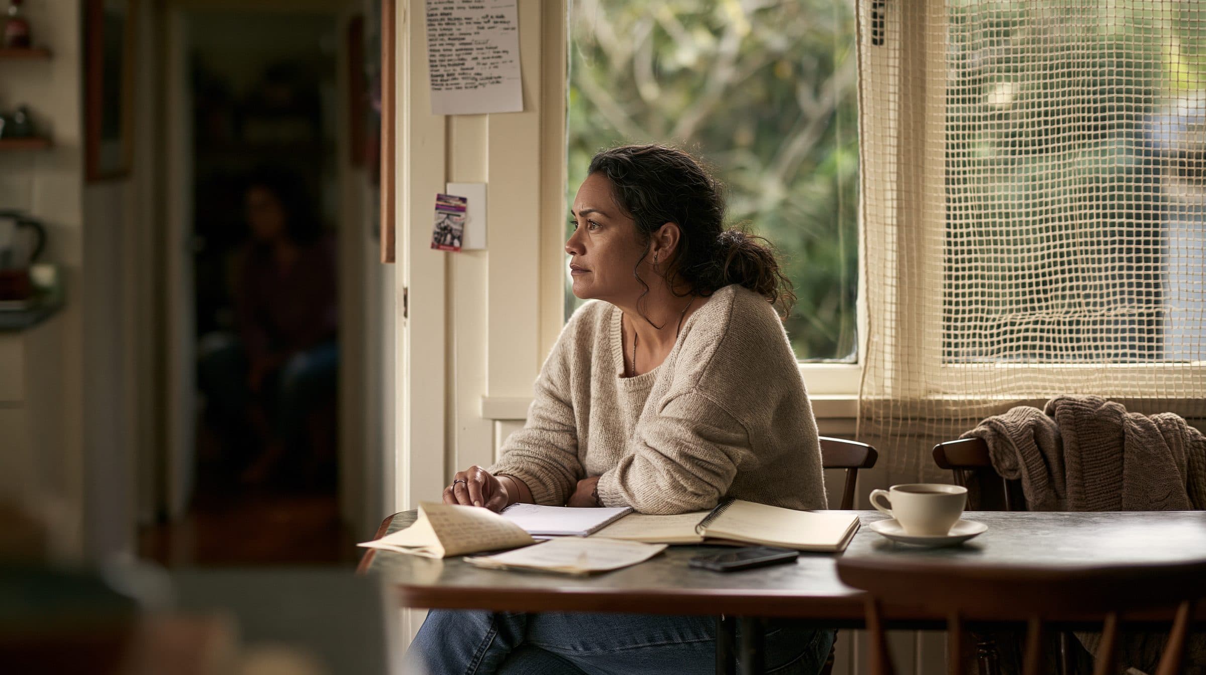 A woman at her kitchen table, letters and notebooks spread out in front of her
