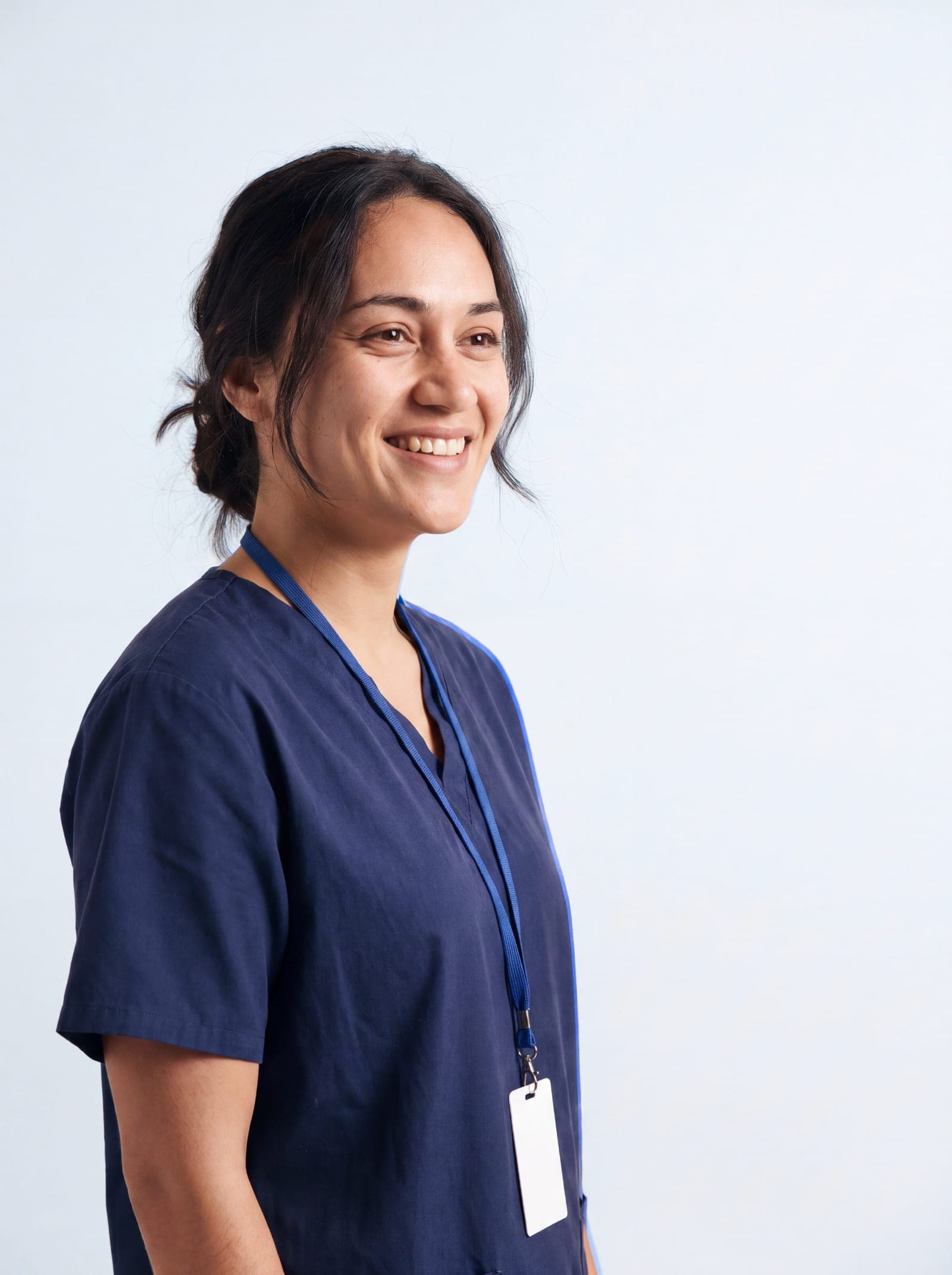 A clinician in navy scrubs wearing a lanyard, looking to camera